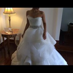 a woman in a white wedding dress standing next to a table with a lamp on it