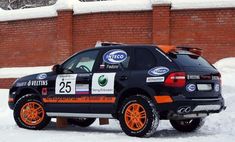 an orange and black car parked in the snow near a brick wall with advertising on it