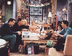 the cast of friends are sitting around a table in front of christmas decorations and presents