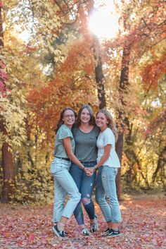 three women are posing for a photo in the fall leaves with their arms around each other