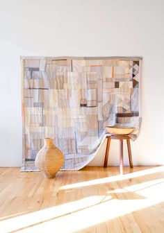 a vase sitting on top of a hard wood floor next to a large wall hanging