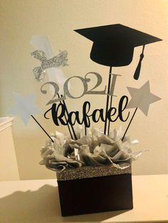 a black and white graduation cake topper in a square box with silver sparkles