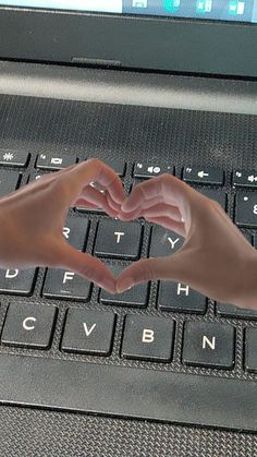 two hands making a heart shape over a laptop keyboard