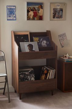 a wooden book shelf filled with books next to a chair and wall mounted pictures on the wall