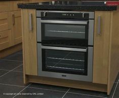 two ovens in a kitchen with wooden cabinets and black counter tops on the floor