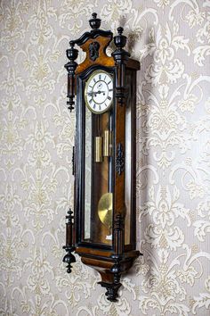 an old grandfather clock hanging on the wall in front of a damask wallpaper