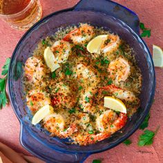 a blue bowl filled with cooked shrimp and lemon wedges next to a glass of beer