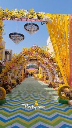 an outdoor ceremony setup with yellow and pink flowers on the aisle, chandeliers hanging from the ceiling