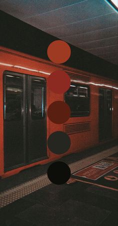 an orange train parked next to a loading platform with circles hanging from it's ceiling