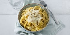 a bowl filled with pasta on top of a blue napkin next to a glass of water