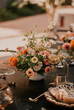 an arrangement of flowers and wine glasses on a table with place settings for two people