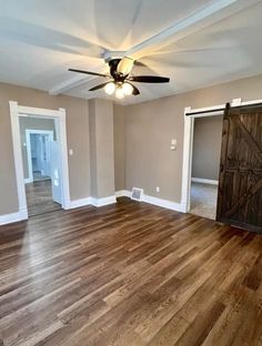 an empty living room with hard wood floors and ceiling fan in the center, looking into the dining room