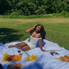 a woman sitting on top of a blanket next to a picnic table filled with food