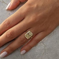 a woman's hand with a yellow diamond ring on her left and white manicured nails