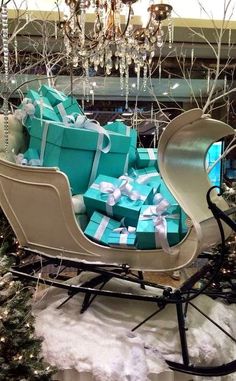 a sleigh filled with presents under a chandelier in the snow next to christmas trees