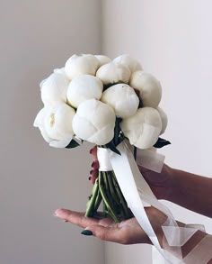 a woman holding a bouquet of white tulips in her hand with a ribbon around it