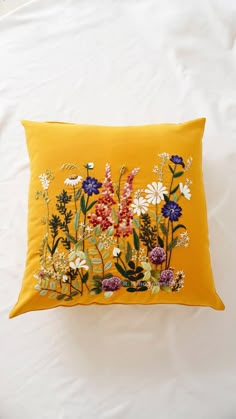 a yellow pillow with flowers on it sitting on top of a white bedding sheet