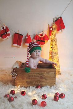 a baby is sitting in a wooden box with christmas decorations around him and wearing a santa hat