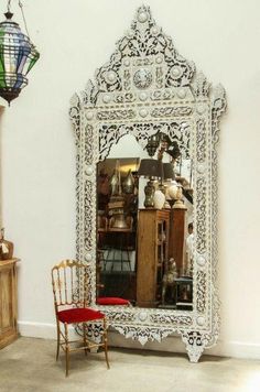 an ornate white mirror sitting next to a red chair