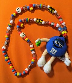 a beaded necklace with a stuffed animal on an orange background, next to it's name tag