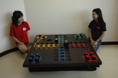 two people playing a board game in a room with white walls and black flooring