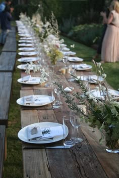 a long wooden table with white plates and flowers