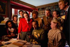 a group of people standing around a table in front of a bookcase with books on it