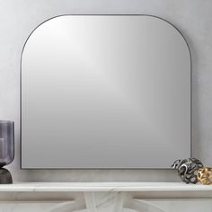 a mirror sitting on top of a white shelf next to a vase and candle holder