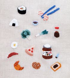 various crocheted food items are arranged on a white cloth surface, including an egg, carrots, and other foodstuffs