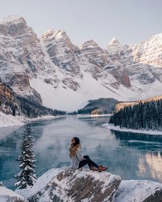 a woman sitting on top of a snow covered mountain next to a body of water