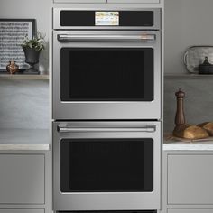 two ovens side by side in a kitchen with white counter tops and gray cabinets