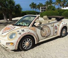 a car made out of shells on the beach in front of some palm trees and bushes