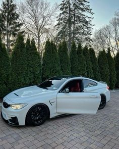 a white car parked on top of a brick road next to some green bushes and trees