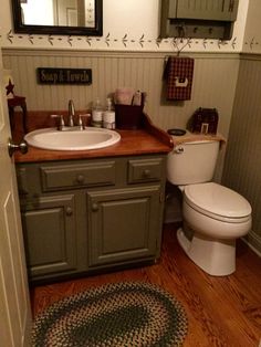 a bathroom with a toilet, sink and mirror in it's corner next to a rug