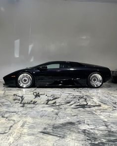 a black sports car parked in front of a white wall next to another one with chrome rims