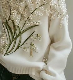 a white sweater with flowers and pearls on it