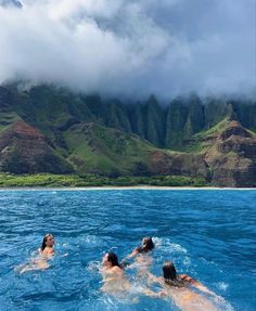 three people swimming in the ocean with mountains in the background