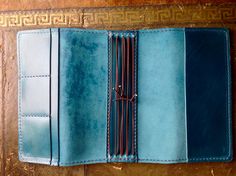 a blue wallet is open on a wooden surface with gold trimmings and stitching