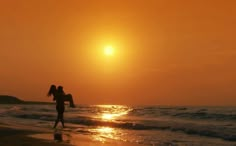 two people are walking on the beach at sunset with their arms around each other as the sun sets