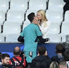 a man and woman kissing each other in front of a stadium full of people with cameras around them