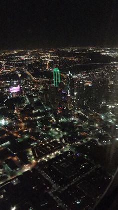 an aerial view of the city lights and buildings at night from inside an airplane window