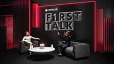 two men sitting on chairs in front of a red and black sign that says first talk