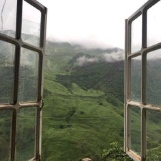 an open window looking out onto a lush green valley and mountains in the distance with fog