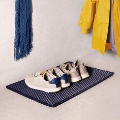 three pairs of shoes are sitting on a mat in front of clothes hanging on the wall