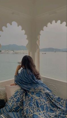 a woman sitting on top of a bed in front of a window next to the ocean