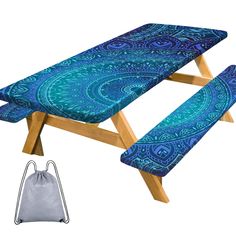 a blue and green patterned table cloth next to an ironing board with drawstring bag