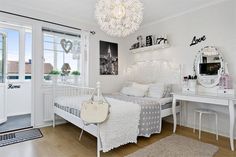 a white bedroom with a bed, desk, and chandelier hanging from the ceiling