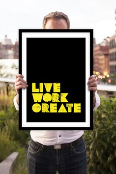 a man holding up a black and yellow poster with the words live work create on it