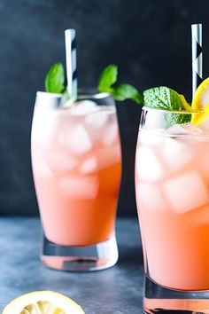 two glasses filled with pink lemonade and mint garnish next to a sliced lemon