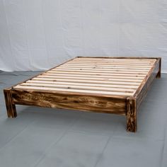 a bed frame made out of wood sitting on top of a white sheeted floor